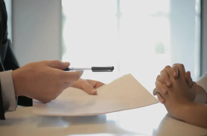 A man and woman sit at a table, engaged in writing with a pen and paper, focused on their task.