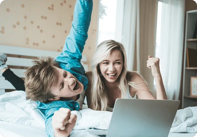 A man and woman lying in bed, using a laptop together, with soft lighting creating a cozy atmosphere.