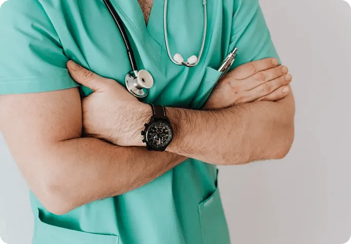 A male physician dressed in a green scrub suit, prepared for medical duties in a clinical environment.